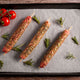 Three lamb skewers of seasoned meat on a baking tray with fresh tomatoes and rosemary.