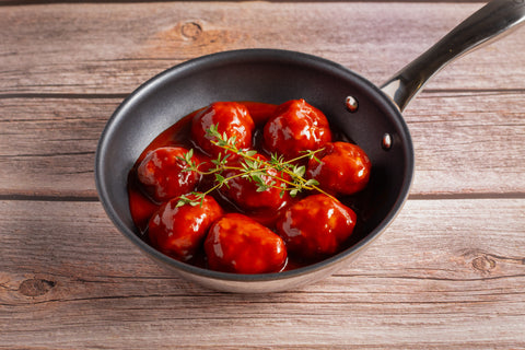 Black skillet with Hugh Maguire Butchers beef meatballs in a red sauce on a wooden surface