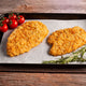 Two breaded chicken fillets on a baking tray with tomatoes and rosemary on a wooden surface